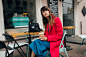 Young attractive stylish woman sitting in city street cafe in red coat drinking coffee wearing blue dress