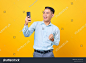 Cheerful young handsome businessman using smartphone and doing victory gesture on yellow background