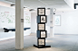 This may contain: a tall black and white display case in an empty room with pictures on the wall