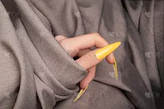 女性手与黄色指甲设计。长指甲。女人手在灰色织物的背景。