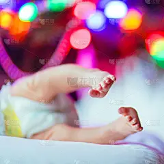 新生儿的脚和尿布的特写与圣诞树和彩色的花环灯在背景下躺在地上显示可爱的小脚。家庭、出生、庆祝的概念