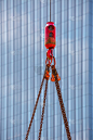 吊车吊钩在钢链和钢丝绳上。背景是一座现代摩天大楼的玻璃幕墙。在建筑工地上装卸建筑材料。发展。