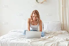 年轻漂亮的金发女人坐在家里使用笔记本电脑