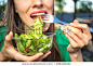 Portrait of attractive caucasian smiling woman eating salad,  focus on hand and fork