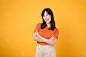 Celebrate confidence with a young Asian woman in her 30s, dressed in an orange shirt, displaying crossed arm sign gesture on yellow background. photo
