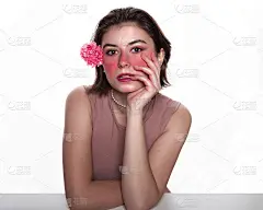 年轻女子带着粉红色的花。随意的女人拿着粉红色的花在耳后，庞大的粉红色化妆品孤立在白色的背景上。概念美