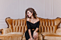 Young, eccentric, interesting woman 25 years old, sitting on large royal chair and posing, against snow-white wall