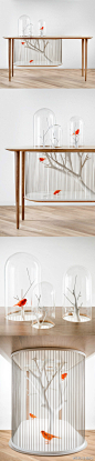 #创意办公家具图酷# 这个鸟笼桌是由美国设计师 Gregoire de Lafforest 设计并制作出来的。它的外观非常的别致，把鸟笼和传统的木质桌子融合到了一起。把鸟笼的主体部分挂在了桌子下面，而在桌子上打孔了三个圆孔并盖上了玻璃罩，这样既不会让鸟飞出来，也给了鸟一些自由飞翔的空间，还能起到展示作用。 