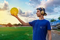 一个十几岁的男孩在一个体育馆里拿着球摆姿势，他手里拿着球，一个绿草如茵的足球场——运动和健康的概念