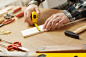 Man working on a DIY project and measuring a wooden plank with work tools all around, hands close up