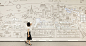 This may contain: a woman standing in front of a wall with a map on it and buildings drawn on it