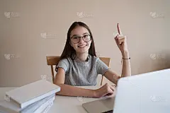 可爱的少女坐在家里的桌子后面做作业。小女孩看着相机，微笑着做第一个手势。