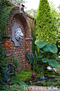 Water splashes from a lion's head set into a brick arch into an aquatic garden brimming with lotus and lilies