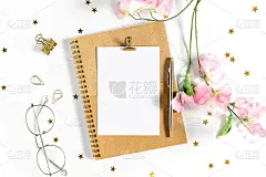 顶视图白色工作台背景与办公设备放在上面。平面放置玻璃，花，金纸装订夹，空白贺卡，工艺笔记本和钢笔。桌