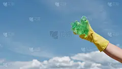 环境问题。在蓝天的映衬下，志工手执黄色垃圾手套，手持废旧塑料瓶