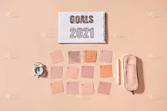 平铺的记事本上写着“2021年目标”、彩色便利贴、时间点、笔和笔盒。颜色粉红色背景
