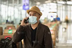 戴口罩的年轻旅行者可以保护流感冠状病毒。一名游客在机场候机楼用智能手机等待航班。在大流行期间必须保持