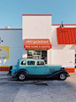 teal and white vintage car parked beside white and red concrete building during daytime