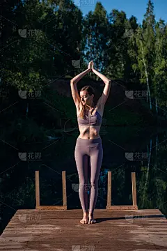 年轻女子在湖边的木铺位上练习瑜伽。在阳光明媚的天气下，对大自然进行单项运动健康训练