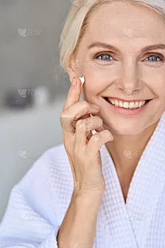 快乐微笑的中年妇女看着相机涂抹面霜。护肤概念。