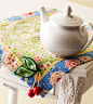 Green, yellow, red, blue floral patterned table mat embellished with wood cherries
