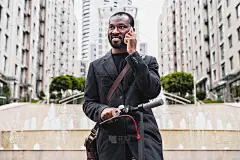 30多岁的非洲男人在户外骑着电动摩托车，一边打电话一边忙着微笑