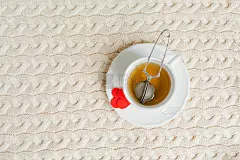 情人节的概念。节日的装饰细节。小小的情人心，热茶杯在编织的背景上。假期。