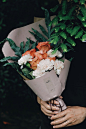 A person holding bouquet of white carnations and pink roses wrapped in decorative paper