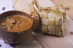 Ketupat(米饭饺子)和咖喱在木制的背景。Ketupat是一种天然的大米外壳，由年轻的椰子叶制成