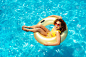 漂亮的年轻卷曲的女孩戴着太阳镜在游泳池里游泳，头顶着充气甜甜圈，抬头看