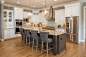 Large transitional l-shaped kitchen in Cincinnati with an undermount sink, shaker cabinets, white cabinets, green splashback, porcelain splashback, stainless steel appliances, medium hardwood floors, with island, brown floor and grey benchtop.