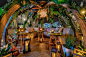 This may contain: an outdoor seating area with lights and plants on the tables, surrounded by greenery