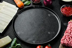 空空间干净盘子烹饪千层面的概念。意大利原料，千层面片肉，香草，西红柿，白汁，在黑色的石头背景，与文本