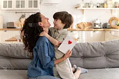 欣喜若狂的妈妈庆祝母亲节拥抱可爱的五岁的儿子，并拿着卡片与小孩子的问候