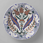 Anonymous | Plate with a Floral Motif, Anonymous, c. 1570 - c. 1590 | Kwarts-fritgoed met lood bord gedecoreerd met tulpen, bloemen in blauw, rood, groen, zwart op wit onder een transparant lood-alkali-tinglazuur.