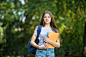 Free photo cheerful attractive young woman with backpack and notebooks standing and smiling in park