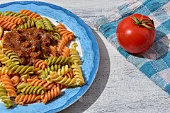 美味的自制彩色意面，肉酱和新鲜的西红柿在白色的木制背景