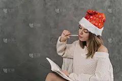 这个女孩为新的一年列了一个愿望清单。送给朋友的礼物清单。戴着圣诞礼帽的女孩在笔记本上写字