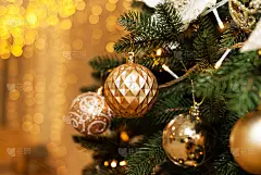 金色的圣诞玩具在圣诞树的树枝上，金色的背景与散景灯。