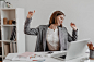 Positive office worker in white shirt dancing while sitting at table on of shelves with documents.