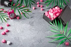 灰色的混凝土背景上是粉色的闹钟、热带树叶、心形的泡沫包装和纸板礼盒。情人节作文，母亲节作文。礼物包装