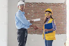土建工程师队伍握手，戴着工作头盔的工人在施工现场。领班工业项目工作工程师团队合作。两个亚洲工程师团队