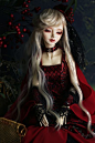 This may contain: a doll with long white hair sitting on a wicker chair wearing a red dress