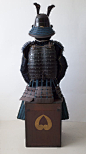 武士大铠。带一个放小旗（指物）的挂包钩 - 日本 - 17 世纪（江户时代） - Catawiki : 深棕色赤胴铠。
有双重胸甲（kurozome nimaido）和五重头盔（zunari-kabuto）。
头盔上带有风格化的飞鹿（锹形虫）角和锥形的前部装饰（maedate），上面有一个红色的”義“字（正义） 
面具为深棕色漆面，带有一个很宽的鼻子（menpo）。 
胸甲的背面带有 gattari 和 machi-uke 用于固定靠旗（指物）。

储存箱带有作为家族徽章的 tomeo-mon 。
储存箱