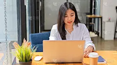 在舒适的办公室里用笔记本电脑工作的白色衬衫的女性肖像