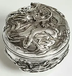 This may contain: a silver box with a dragon design on the front and sides, sitting on a white surface