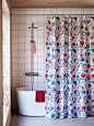 A bathroom with a KRATTEN shower curtain in white and multicolour, pulled partly back to display a bathtub and a shower.