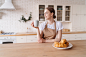 Free photo young beautiful woman in the kitchen in an apron with coffee and croissant enjoys her morning