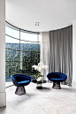 A black lacquer ClassiCon 'Bell' side table sits between a pair of Knoll 'Platner' chairs in blue velvet. The curved lines of the furniture echo the curved steel-framed window in this section of the living room | Photography: Jack Lovel