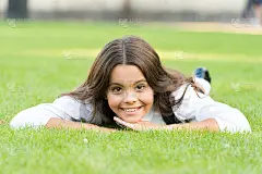 保持冷静，放松。快乐的孩子带着学校的样子躺在绿色的草地上。小女孩微笑着，穿着正式。小学生的美貌